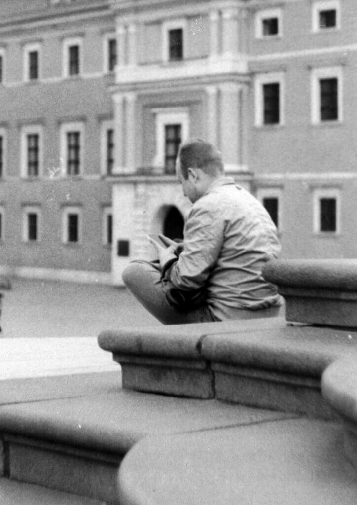 Czarno-biała fotografia mężczyzny piszącego w notesie na kamiennych stopniach w Warszawie